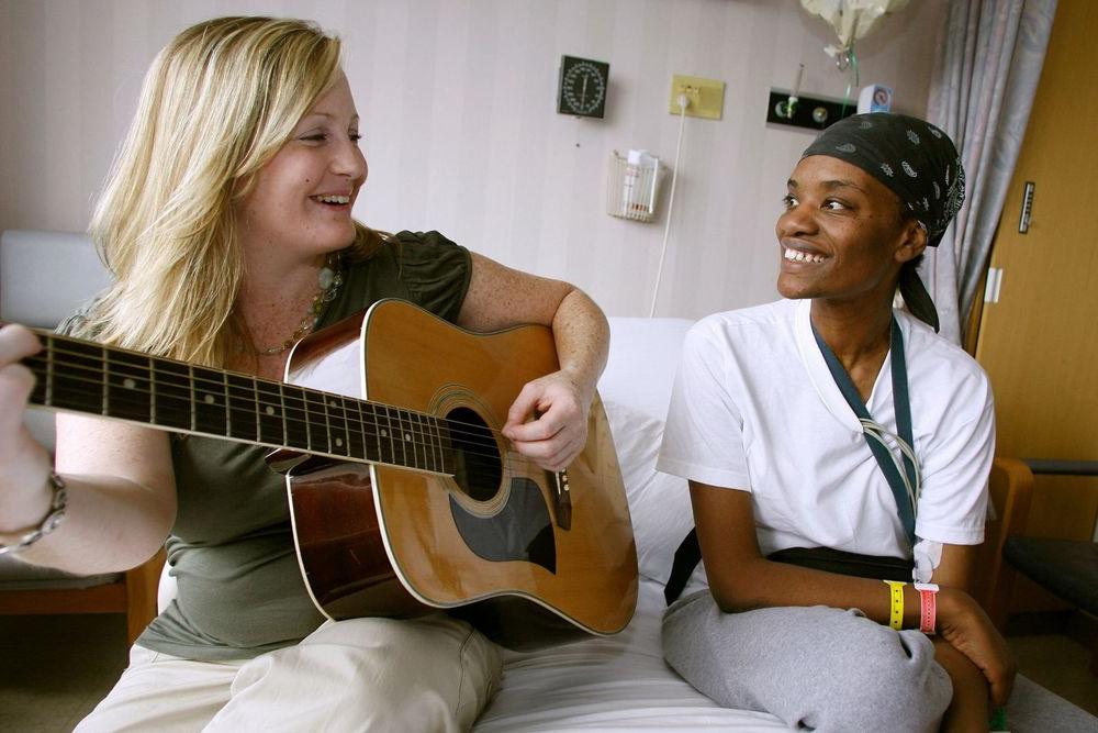 一个音乐治疗的学生坐在病床上，旁边的病人一边弹吉他.